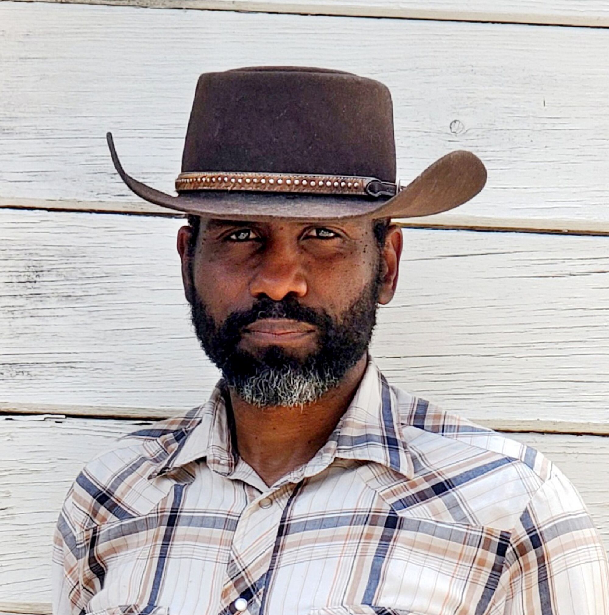 A square head-and-shoulders of Hop Hopkins wearing a checkered shirt and a leather hat.