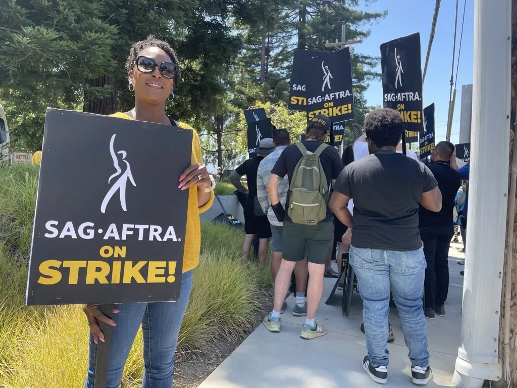 An African American woman holds a SAG-AFTRA on STRIKE sign with protestors behind her holding the same signs.