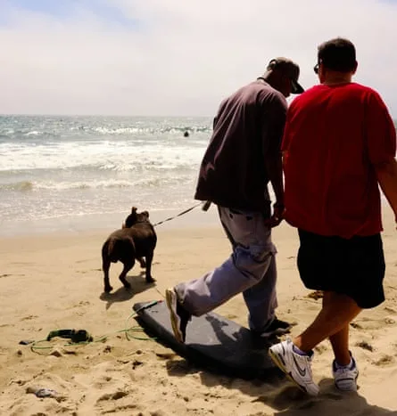 Two men and their dog walking along the shore at Santa Monica Beach.