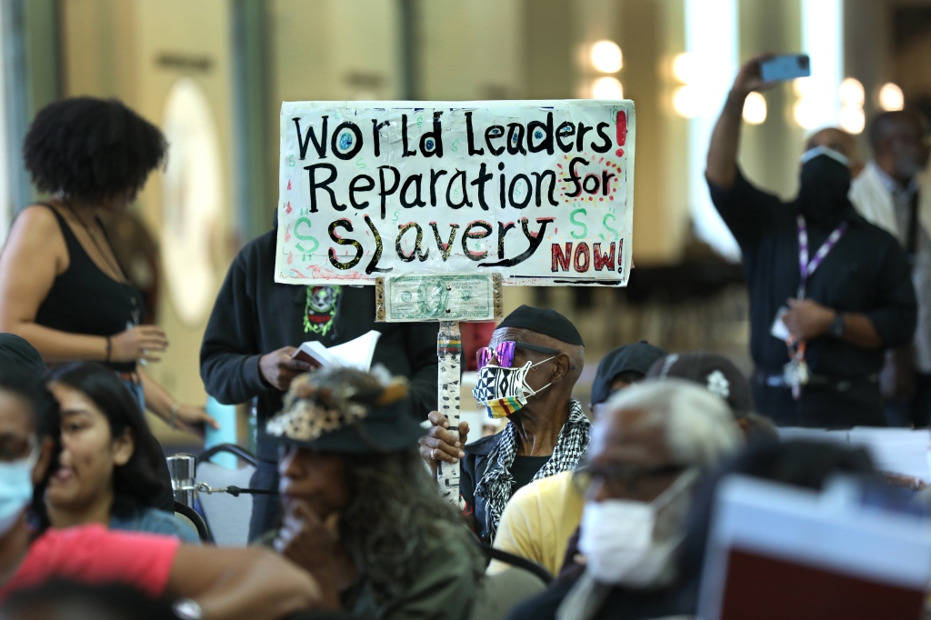 Walter Foster, 80, holds up a sign as the state Reparations Task Force meets.