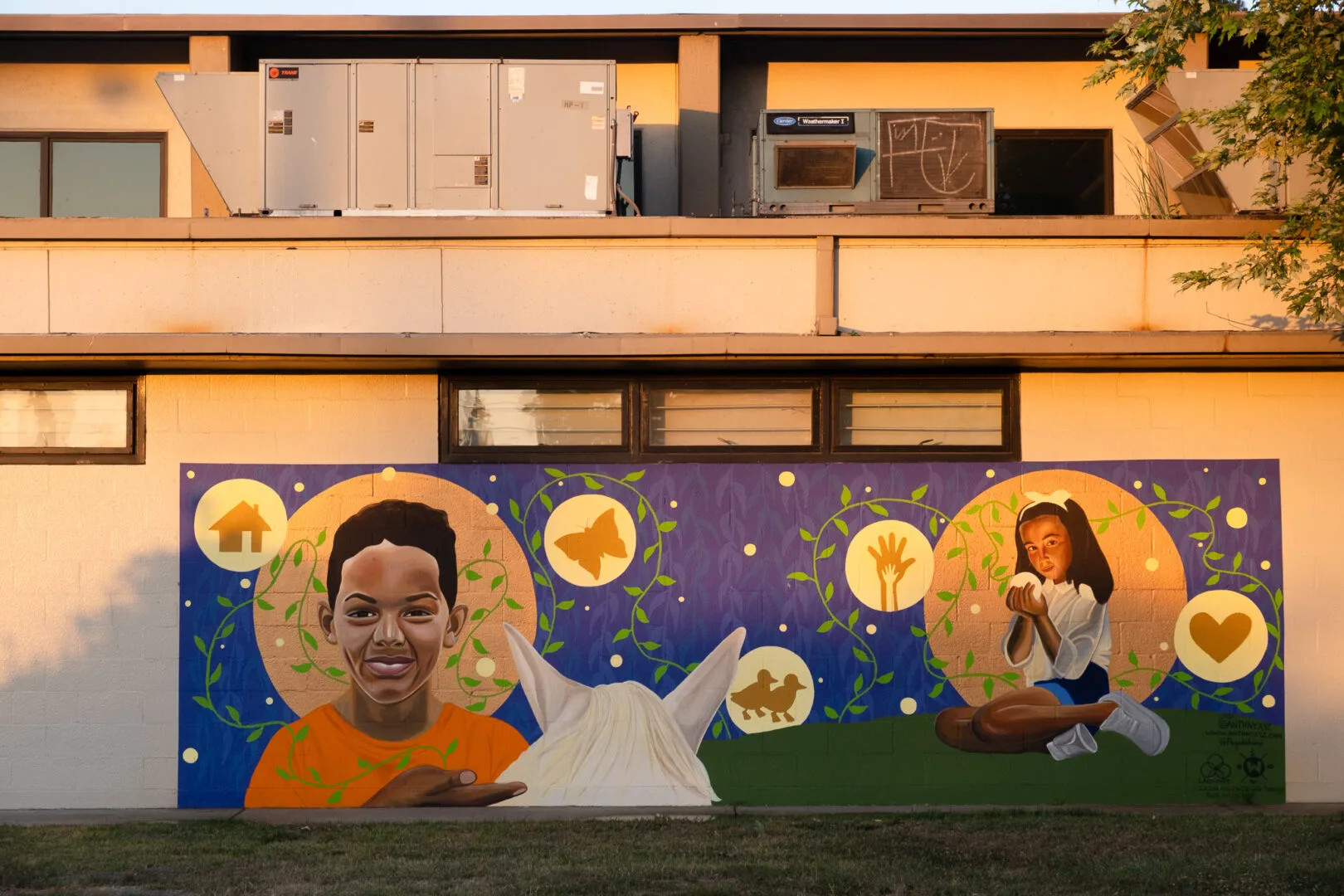 A mural depicting a young boy playing with a horse and a young girl holding a ball of light. There are drawings of a house, a butterfly, a hand, and a heart. An air conditioning unit sits above.