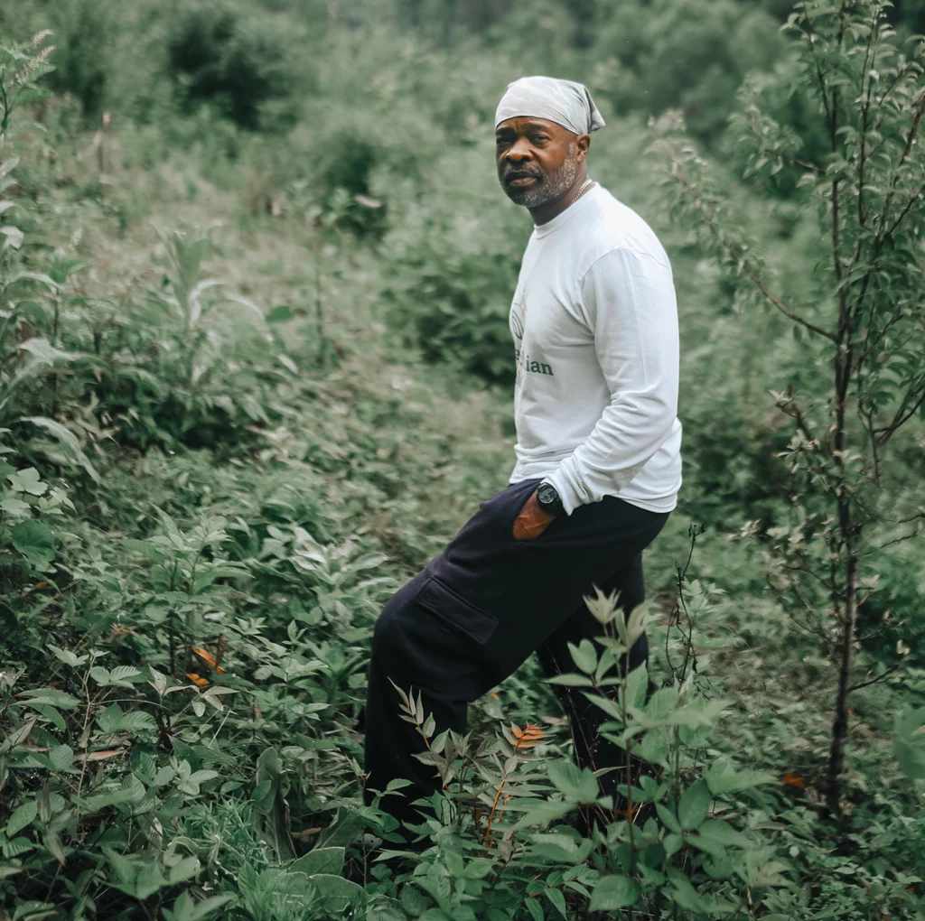 Jason Tartt looks directly at the camera as he stands among a fruit tree orchard on his sustainable farm in Vallscreek, West Virginia.