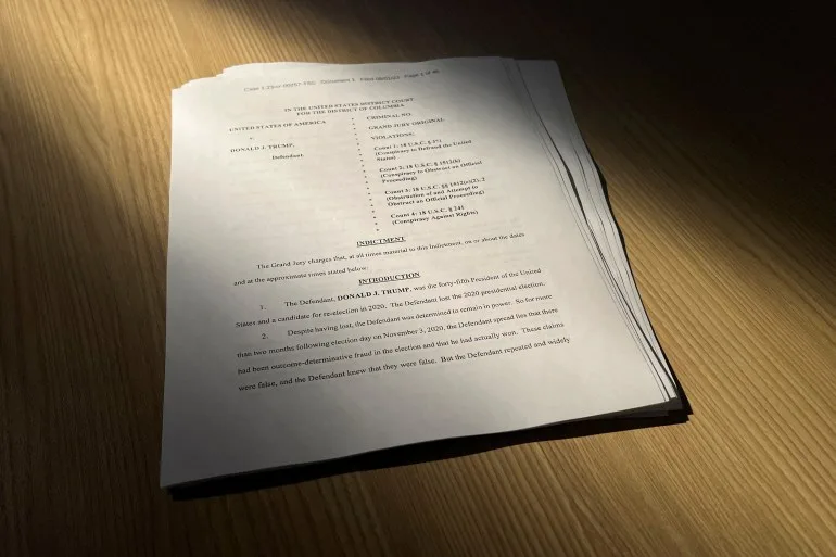 A stack of papers from the August 1 indictment are seen on a wooden table.