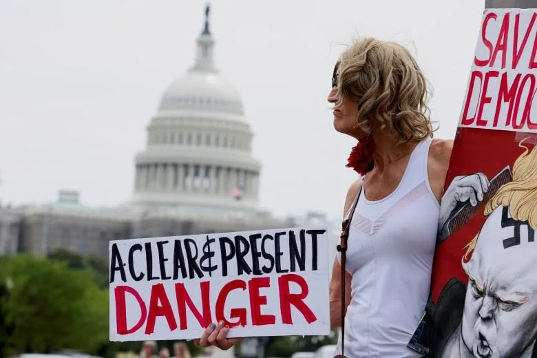 Protester holds sign calling Trump 'A clear and present danger', with Capitol building in the background 