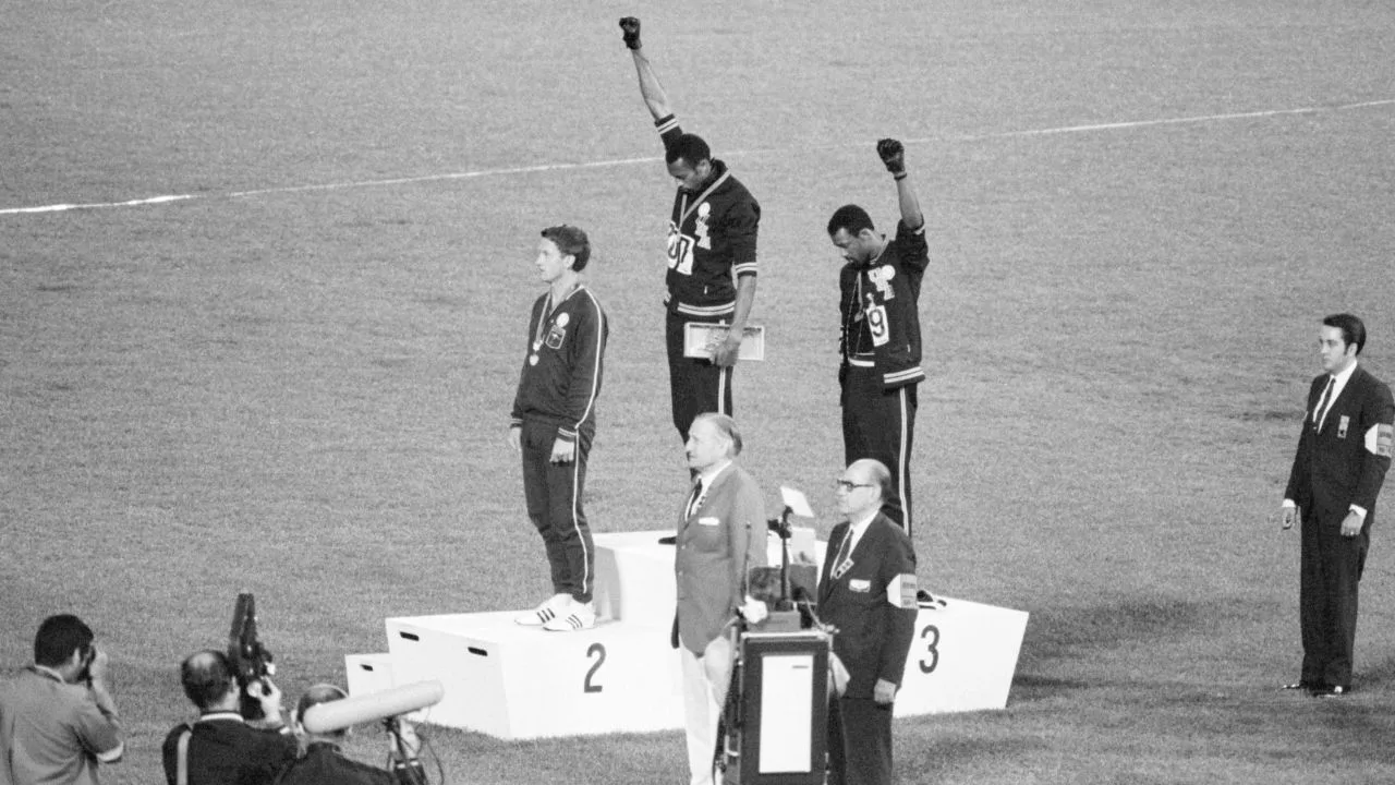 Tommie Smith and John Carlos, gold and bronze medalists in the 200-meter run at the 1968 Olympic Games, engage in a victory stand protest against unfair treatment of blacks in the United States. With heads lowered and black-gloved fists raised in the black power salute, they refuse to recognize the American flag and national anthem. Australian Peter Norman is the silver medalist.