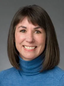 This is a photo of Cari Boyce, a lottery commission member. She is a middle-aged white woman with brown hair that is just above her shoulders. She's wearing a blue turtleneck.