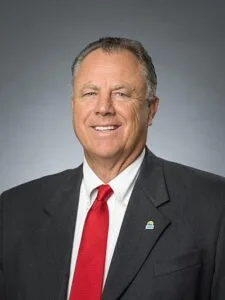 This is a photo of lottery commission member Randy Jones. He's white man with gray-black hair. He's wearing a dark blue suit jacket, red tie and white dress shirt.
