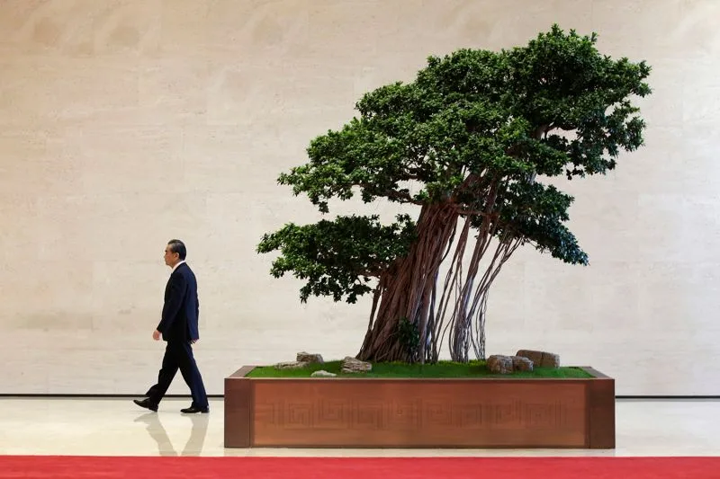 Chinese Foreign Minister Wang Yi, seen in a suit and tie and in profile, walks outside the venue at the Belt and Road Forum for International Cooperation. Behind him is a sculptural tree in a larger planter that appears to be leaning away from him.