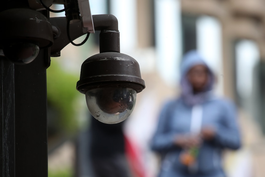 A surveillance camera hangs from the side of a building