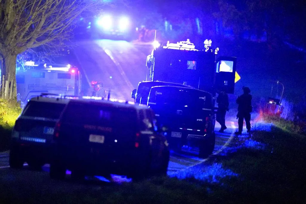 Law enforcement officers, right, stand near armored and tactical vehicles, center, near a property on Meadow Road, in Bowdoin, Maine, Oct. 26, 2023. 