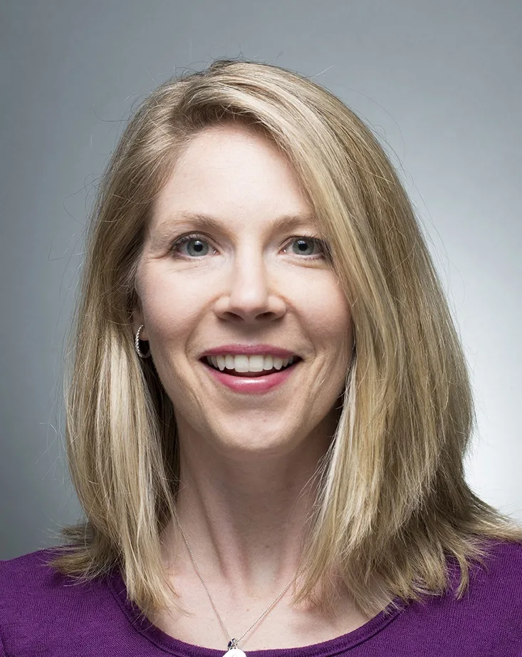 Mia Pritts headshot: white woman in blue shirt smiling against grey and white background