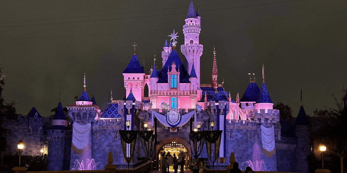 Sleeping Beauty Castle at night after the rain with pink lights and the Disney100 decorations in Disneyland Park at Disneyland Resort