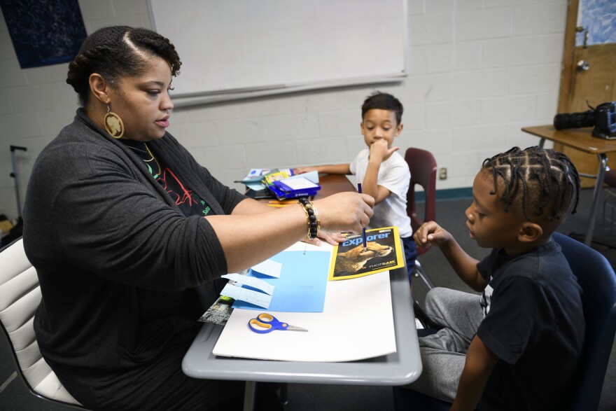 Teacher Angela Mitchell guides Enzo Irbyr and Terrel Nemons as they recreate their own Black Wall Street in paper form.