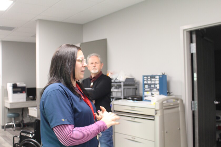 A man in a black shirt and pants listens to a woman in blue scrubs during a medical center tour.