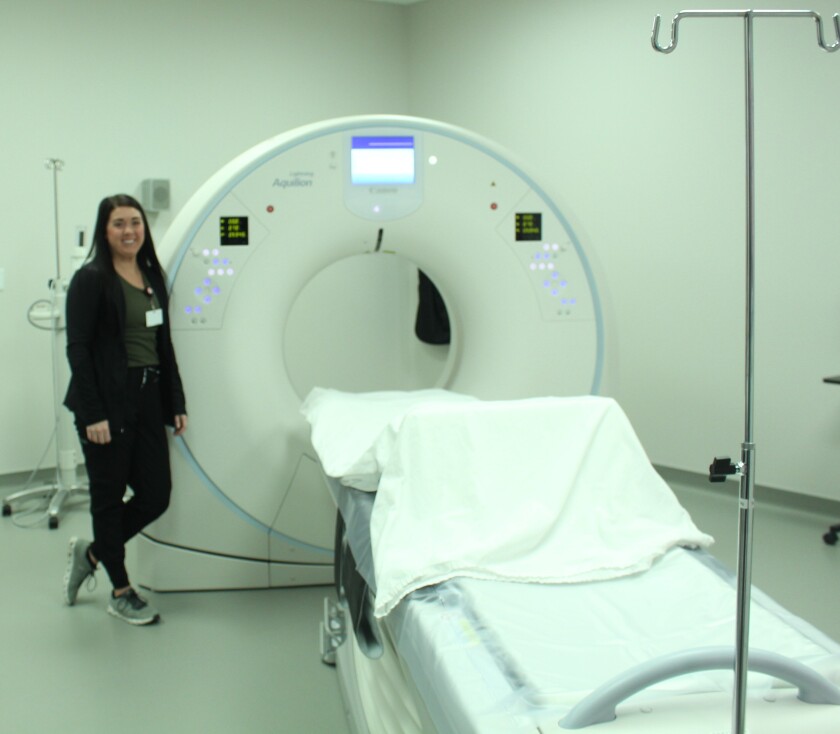 A woman in black scrubs stands by an MRI machine.