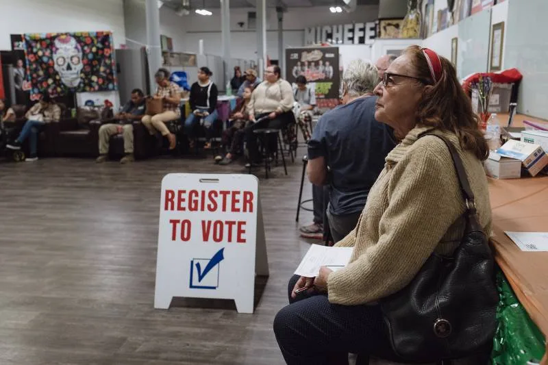 A side view of a woman wearing glasses seated next to other people with a sign that reads 