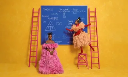 Amanda Gorman up a ladder writing equations on a blackboard, next to which stands Margot Lee Shetterly