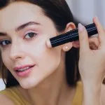 Concealer stick. Charming beautiful woman using concealer stick while putting makeup on