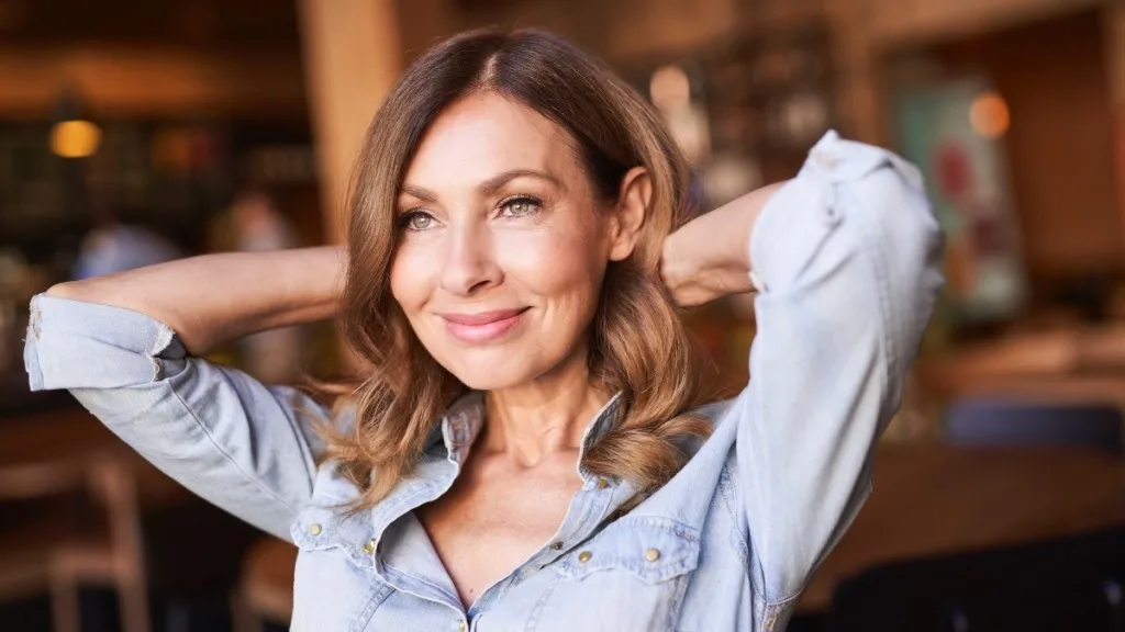 A woman in a chambray shirt with her hands behind her head, who used black seed oil for her hair