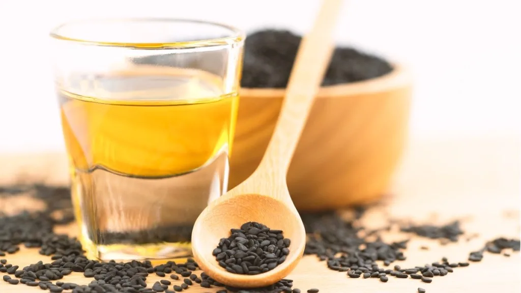 Black seed oil in a glass cup next to seeds, which is used for hair growth