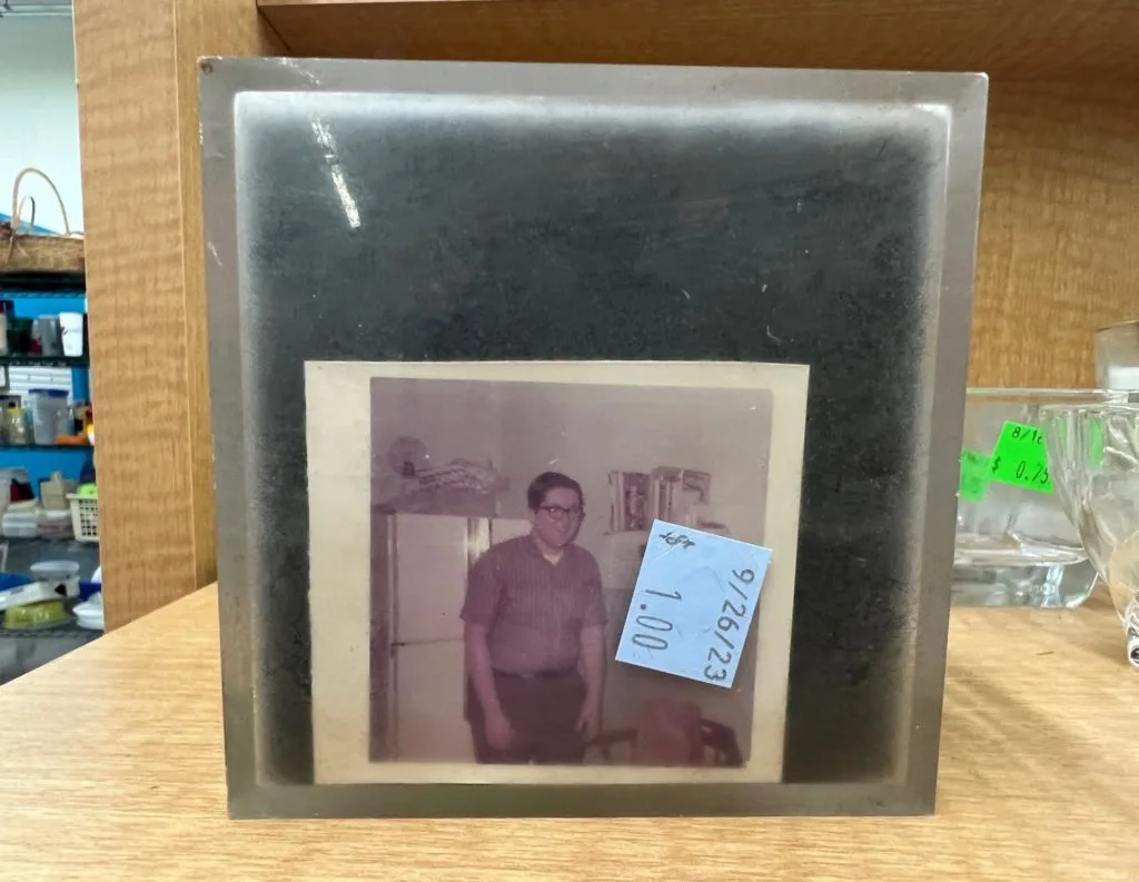 A plastic photo cube with an old photo of a young man with glasses slid into one side.