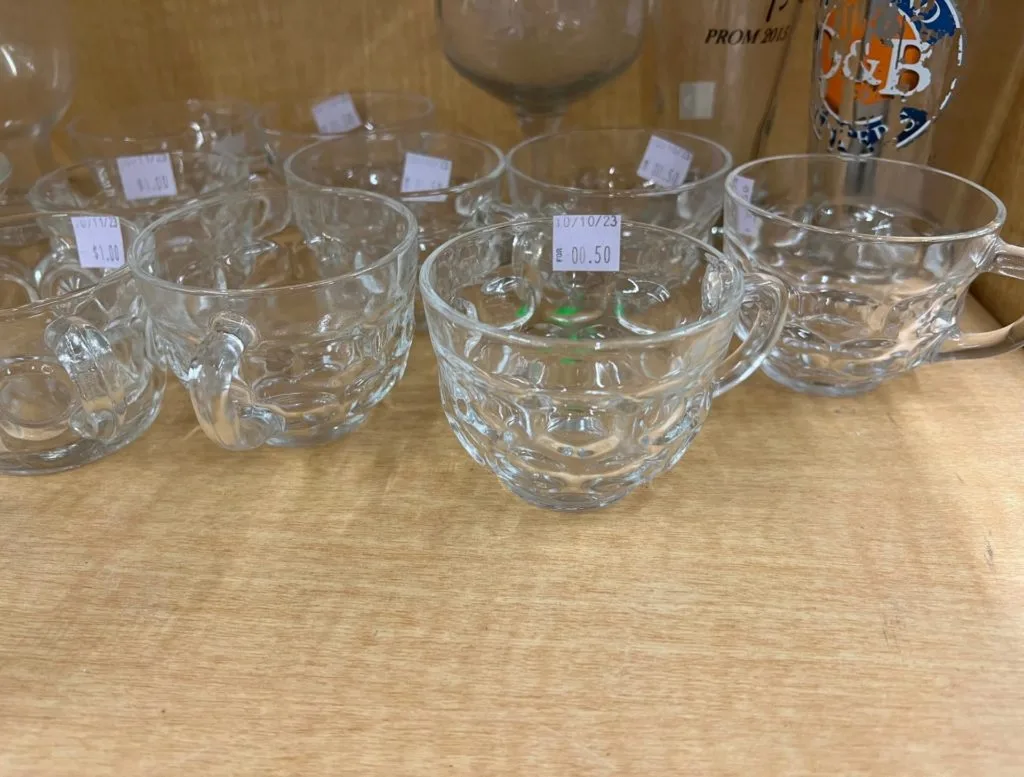 A collection of small glasses with handles sitting on a wooden shelf. 