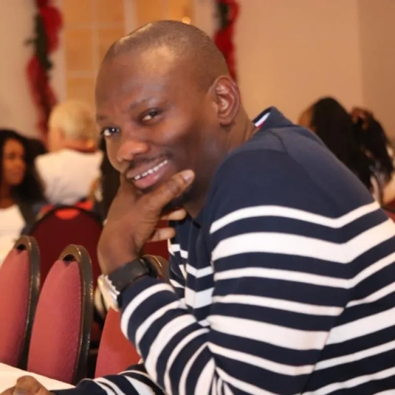 Black man wearing navy and white stripe sweater smiling at camera with his hand under his chin.