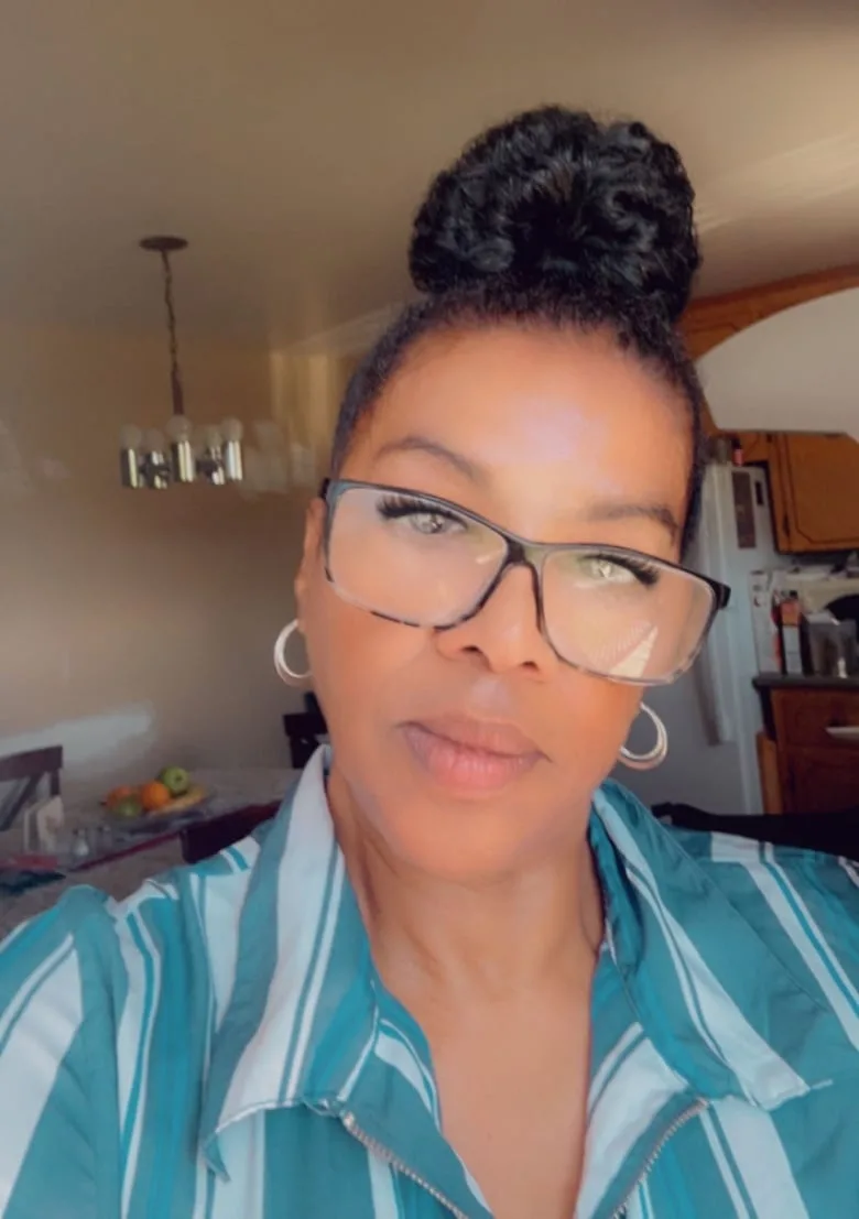 Black woman with dark hair in a bun and large frame black glasses wearing a turquoise stripe bloused.