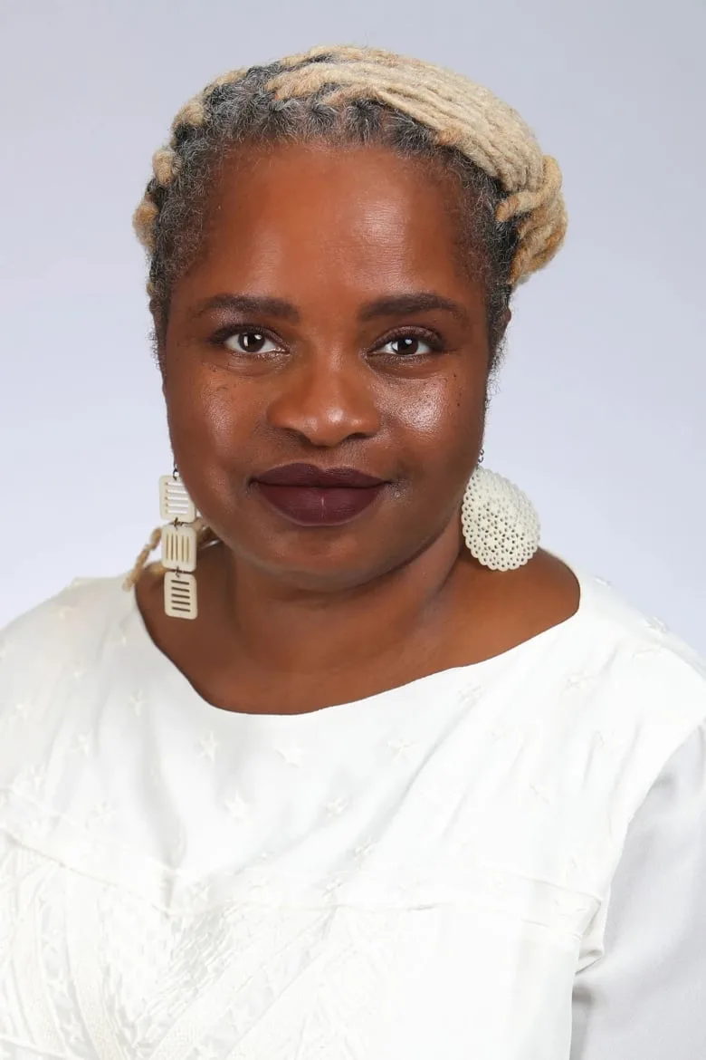 Black woman wearing a white shirt and long silver earrings smiles into camera. 