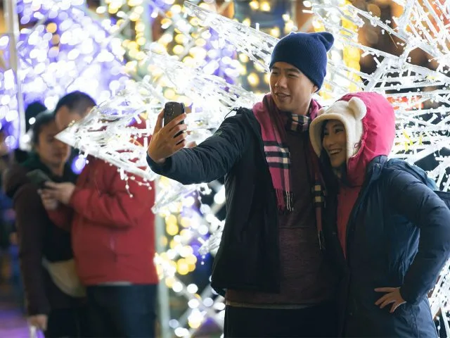 A couple poses for a selfie in front of a winter-themed light sculpture.