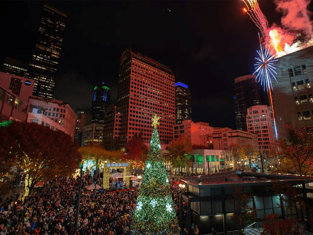 Aerial view of the Tree Lighting Ceremony at Westlake Plaza.  In the foreground, a lit Christmas tree.  To the right, the illuminated Macy's star, with fireworks launching off the Macy's building.