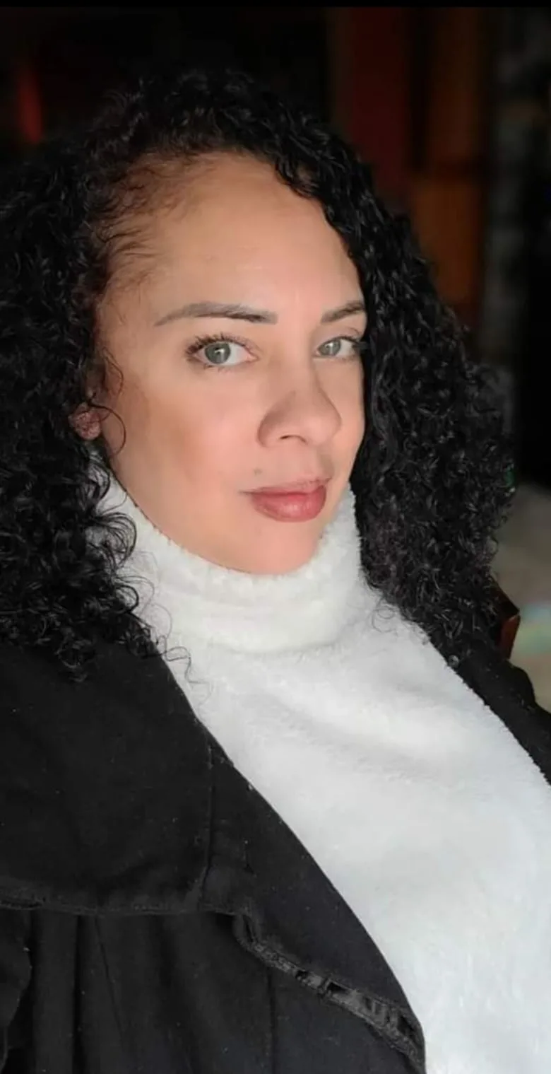 Black woman with curly long hair wears white turtle neck and black jacket