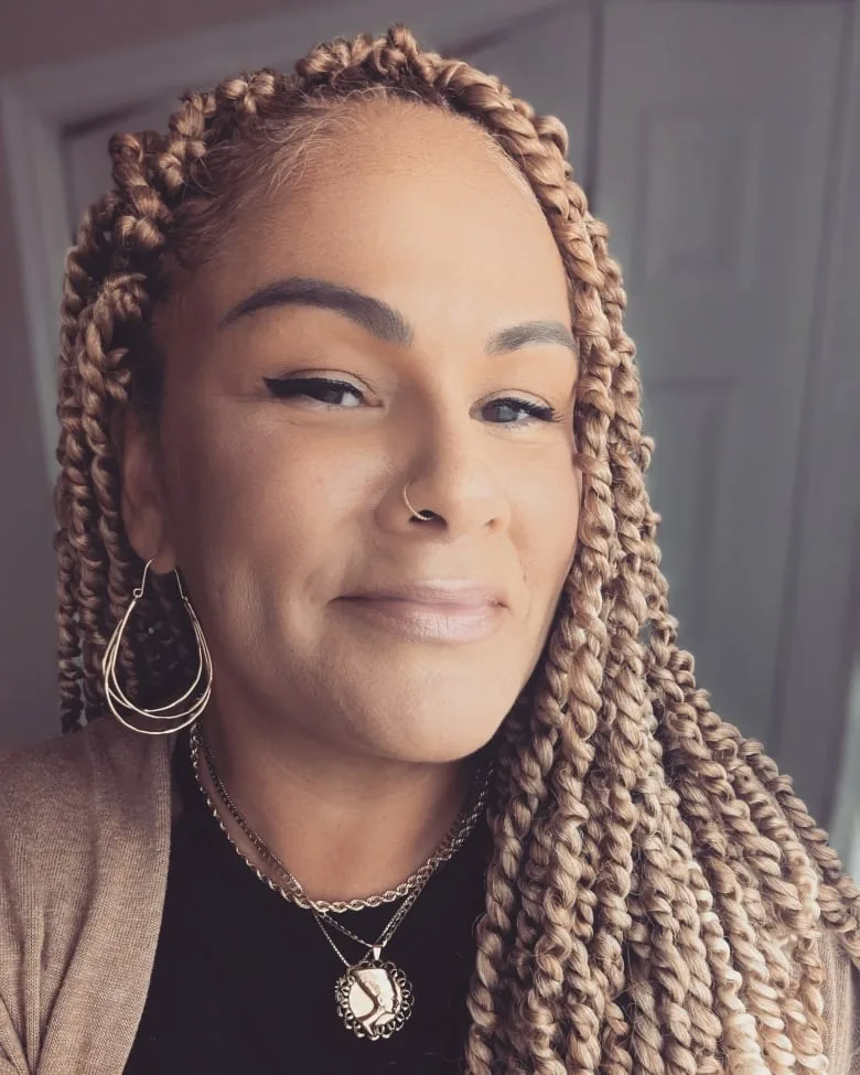 Black woman with long twists, nose ring and hoops earrings and black shirt smiles at camera.