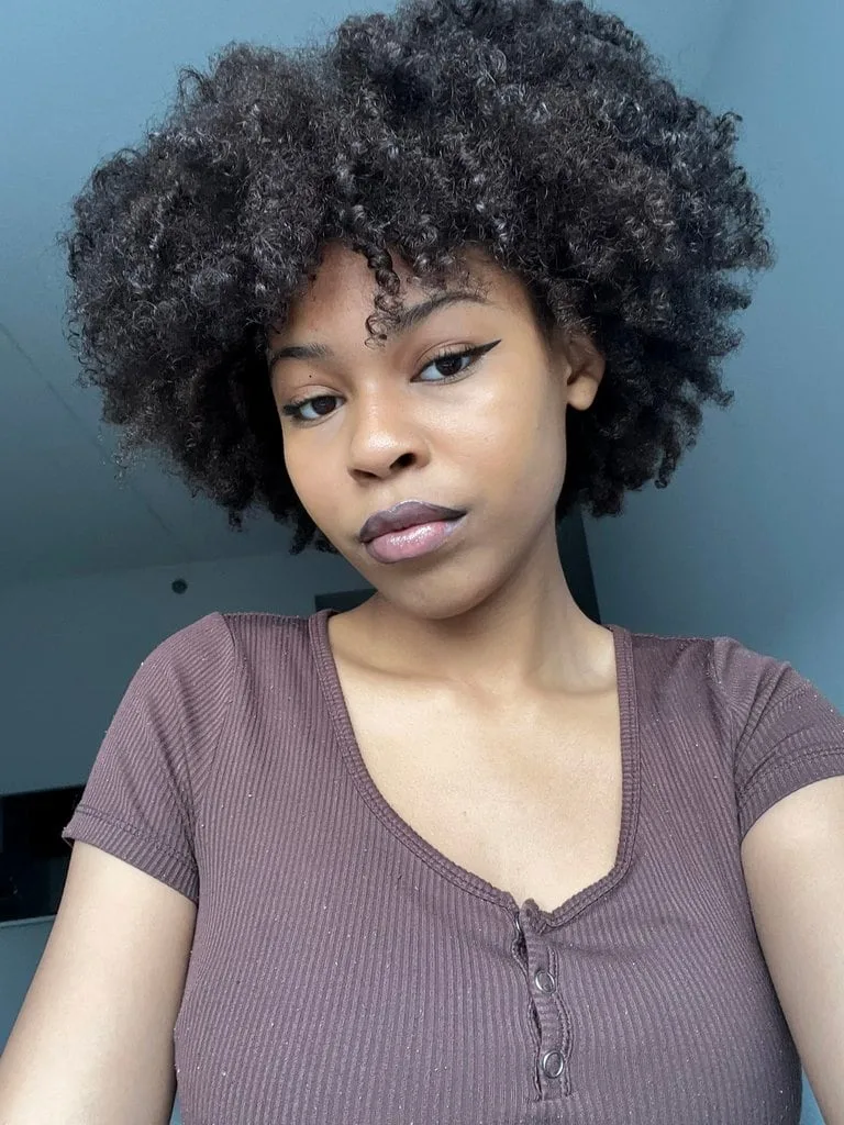 A young girl with black, curly hair wearing a purple shirt poses for a photo.