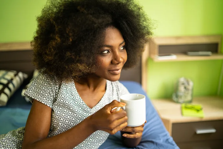 Close up of a woman holding coffee mug lying in bed