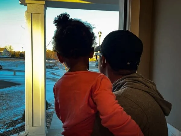 A woman holds a child as they stand in a doorway