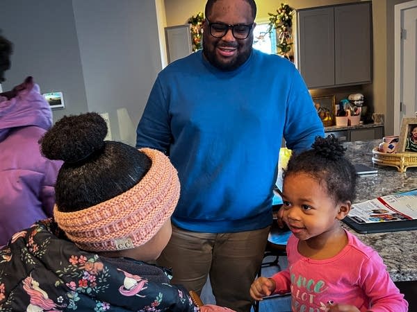 A man watches two girls say goodbye to each other in a kitchen