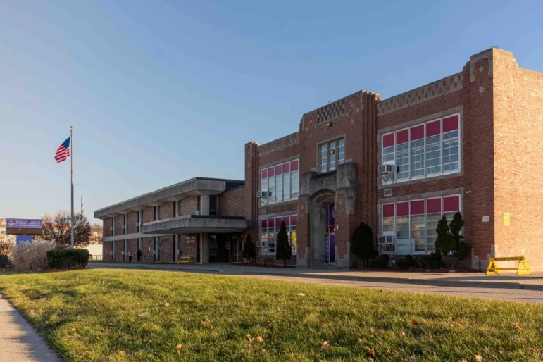 Brown & Black girls support Working on Womanhood: Long shot of traditional, two-story, red brick building with many windows, set back behind a driveway and green lawn.