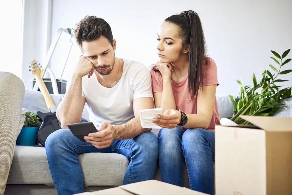 serious couple sitting on couch in new home checking bills