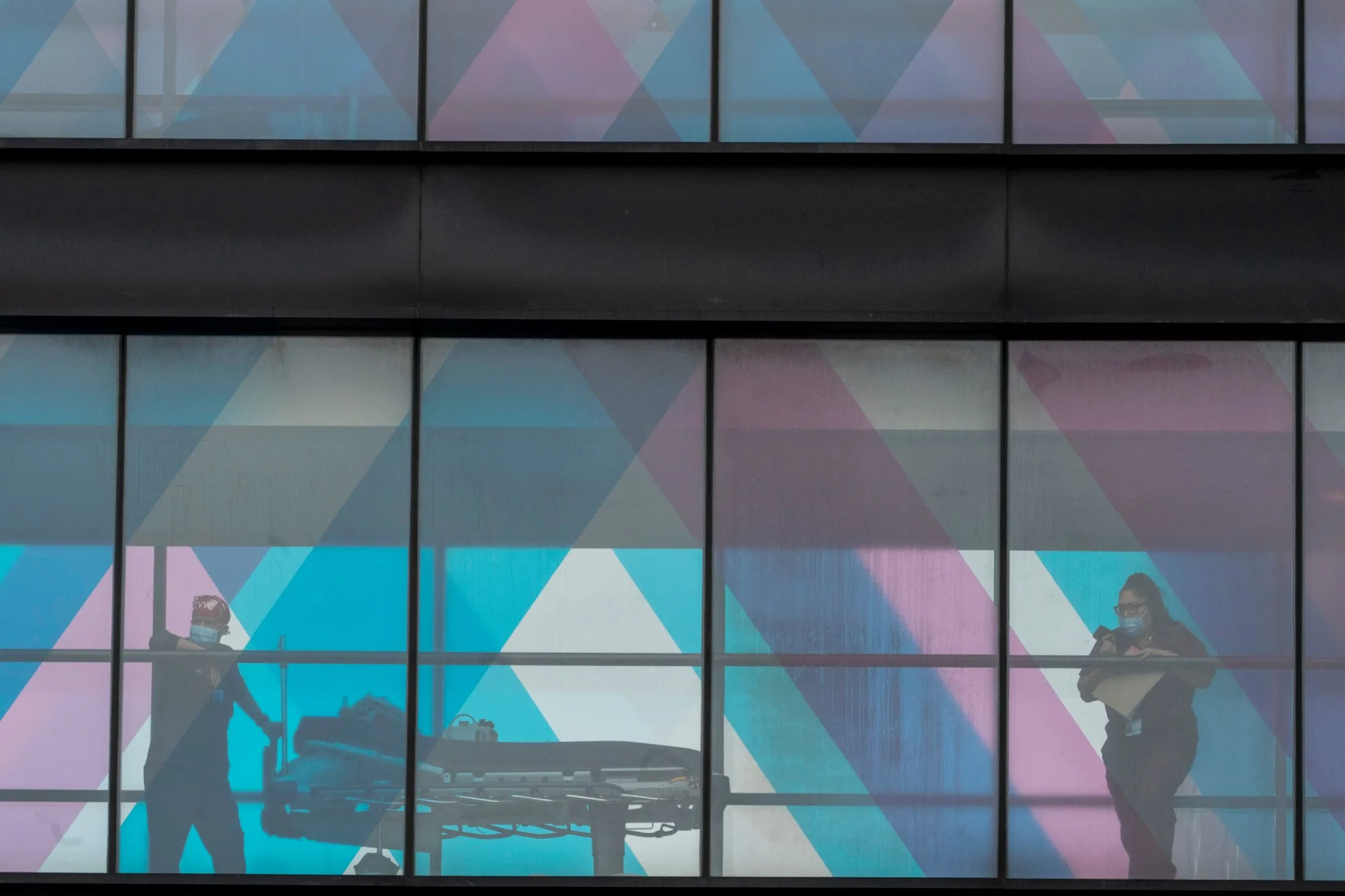 Health care workers look out the window at NY Presbyterian and Mount Sinai from an overpass at Mount Sinai Hospital, Tuesday, March 16, 2021, in New York.