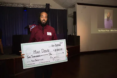 A person at a Fresno Metro Black Chamber of Commerce event holds an oversized check for $2,000 for a pitch competition. 