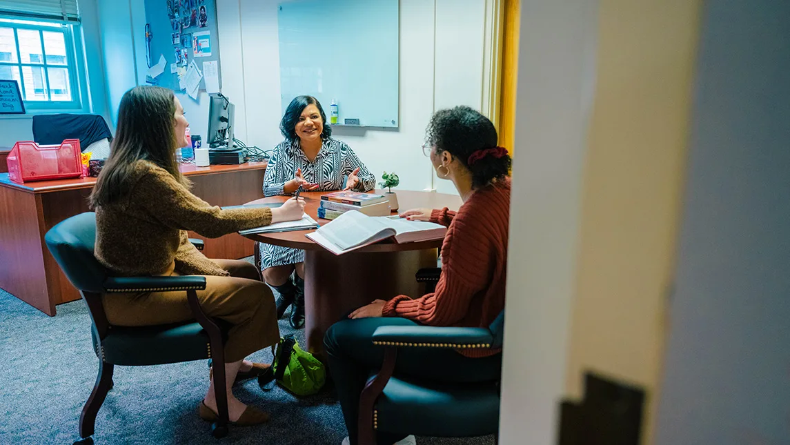 Three people sit around a table in an office environment.