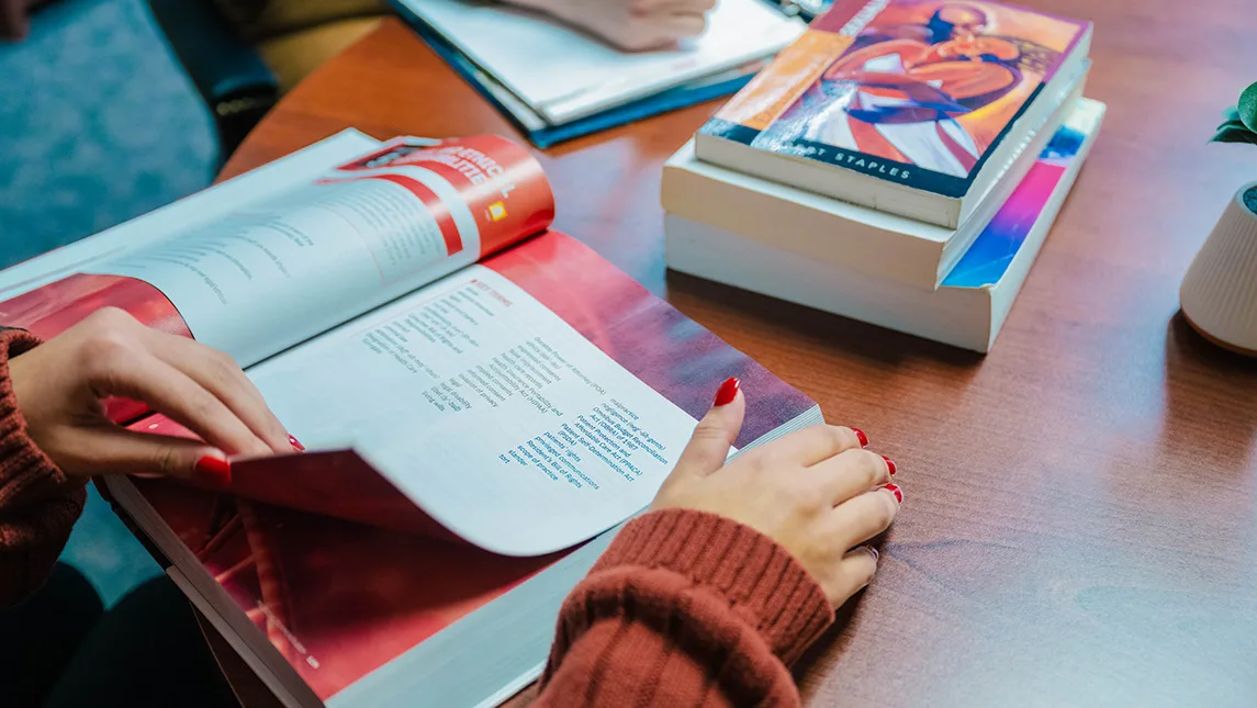 A close-up photograph of a textbook with a person's hands flipping the pages