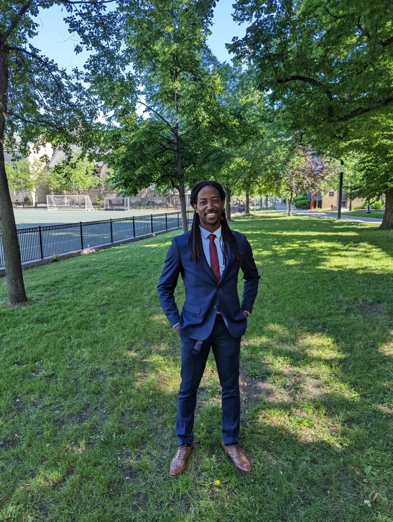 Man in black suit stands outside on the grass.