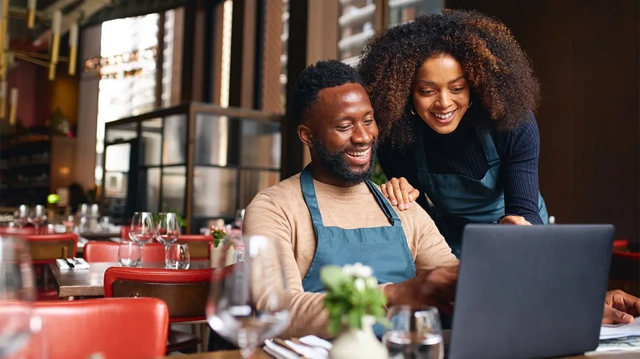 Small business owners in a restaurant smiling at their computer screen.