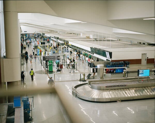 A view from above of a baggage carousel in the foreground and people walking through an airport in the distance. 