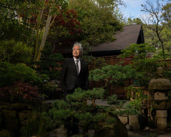 A man stands in a garden that includes a bonsai tree.