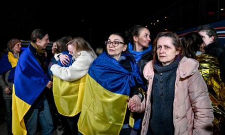 Women, some draped in blue and yellow Ukrainian flags, are greeted with hugs 