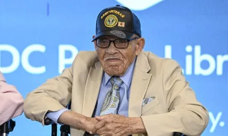 Older Black man with military cap and beige suit sits in wheelchair.