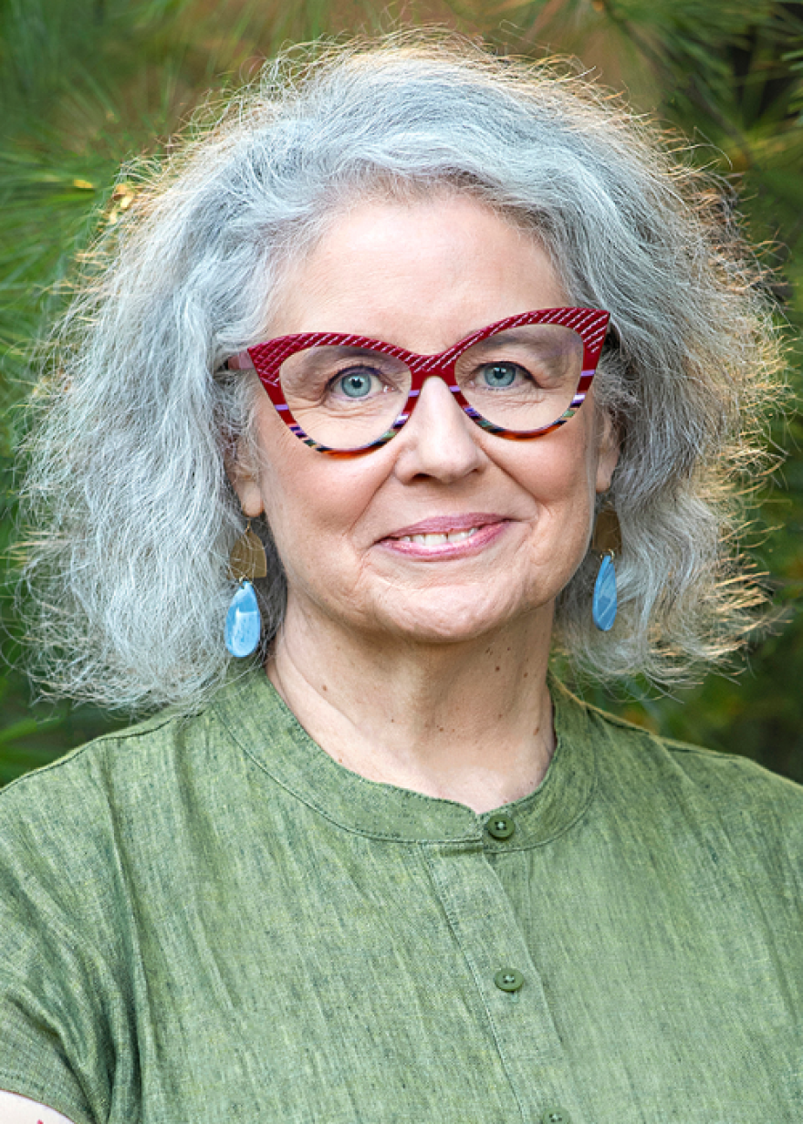 A head shot of Arline Geronimus in a green shirt with glasses and gray hair